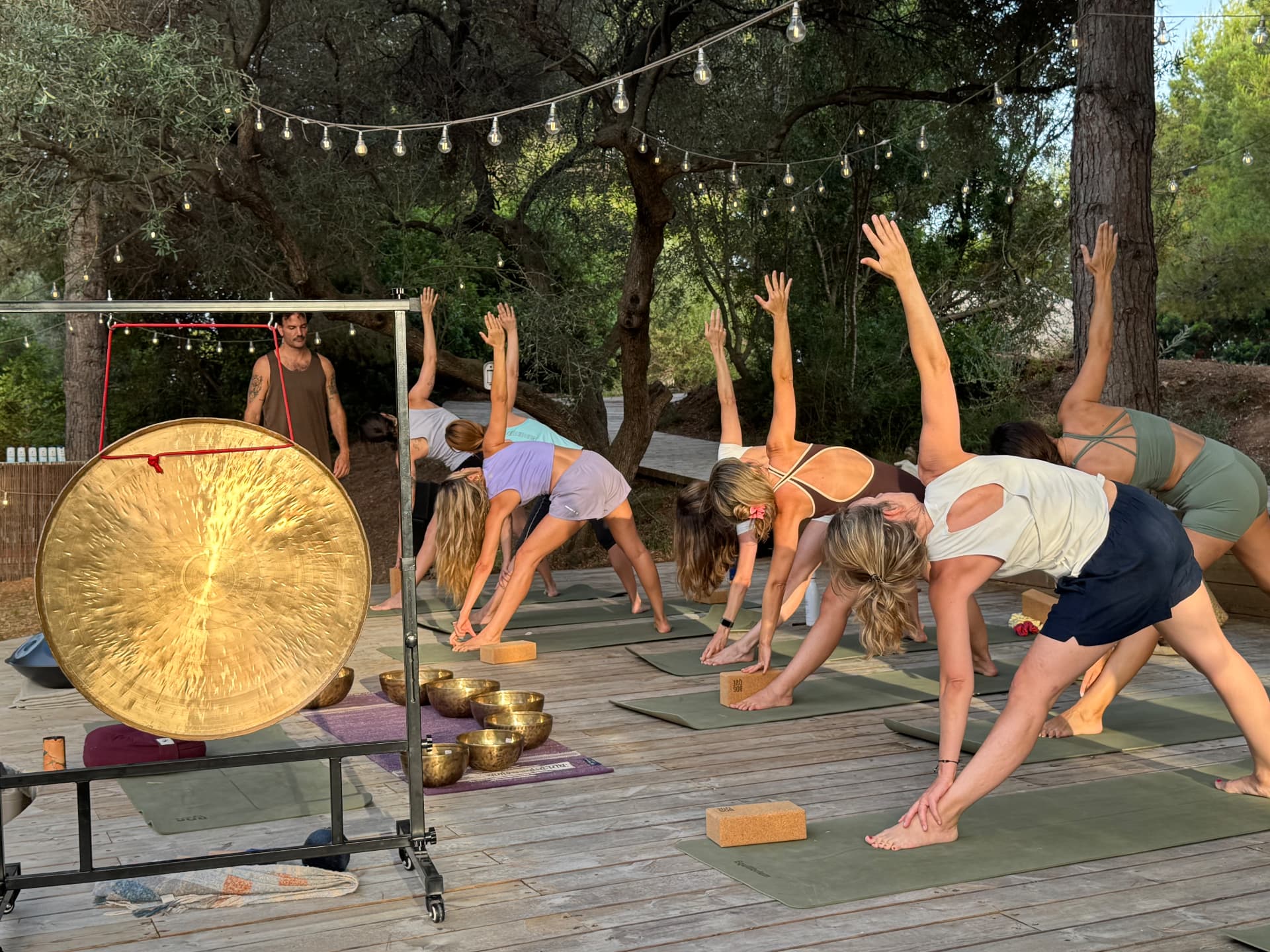 Sesión de yoga con gong sobre la plataforma de madera de Bosque Masía Bellver, entre pinos