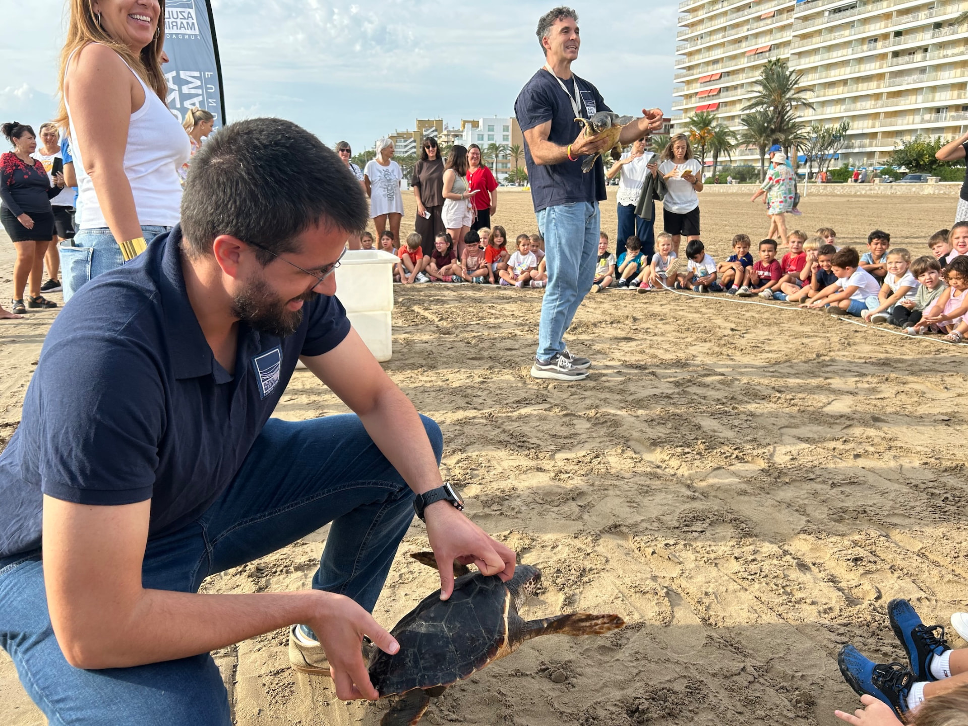 Biólogos de la Fundación Azul Marino sueltan tortugas bobas en la Platja Nord de Peñíscola ante escolares sentados en la arena