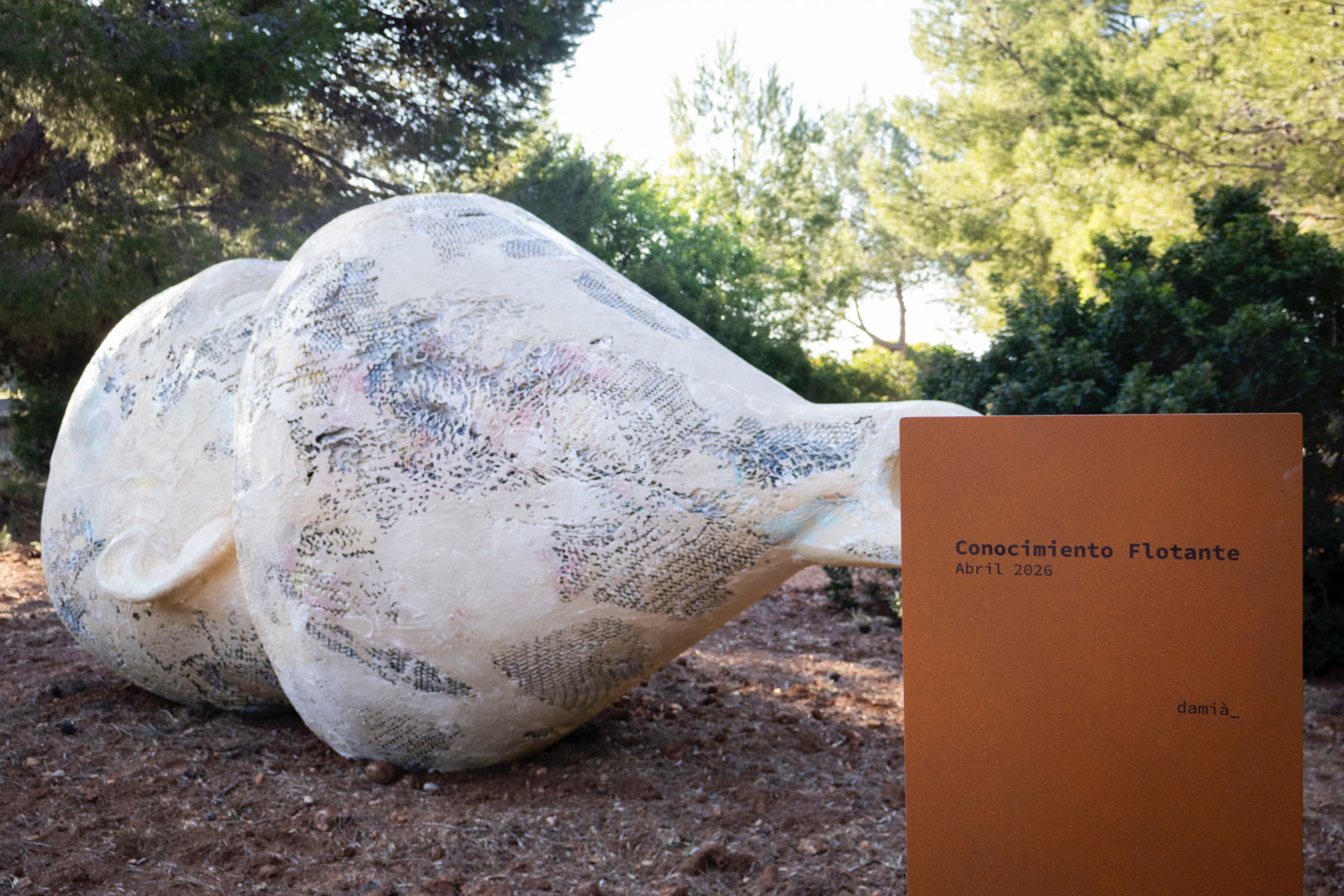 Escultura terrestre de Conocimiento Flotante, de Damià, entre pinos en Bosque Masía Bellver, junto al cartel de la obra