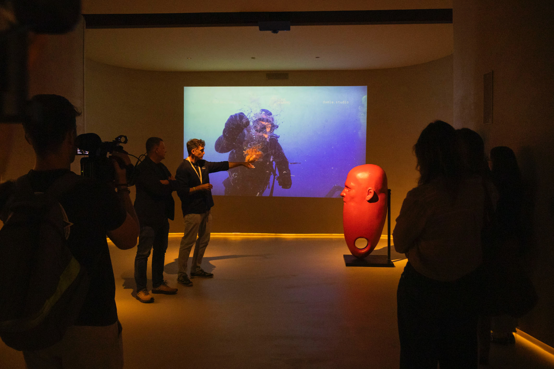 Visita guiada frente a una proyección submarina, con una escultura roja de Damià en primer plano